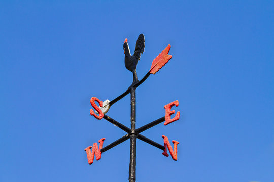 Cockerel Rooster weather vane, wind vane, weathercock against blue sky. Antique cast iron wind direction instrument, with letters for compass points, painted black red and white. Dublin, Ireland