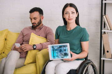 young disabled woman showing digital tablet with dna information app while sitting near boyfriend using smartphone