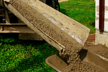 Workmen team in the process of forming foundation blind area. Concrete works with mixer truck and people with wheelbarrow. Labour builders at construction site filling formwork with  cement and gravel