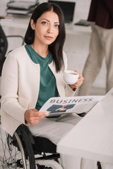 attractive disabled businesswoman holding coffee cup and newspaper while looking at camera