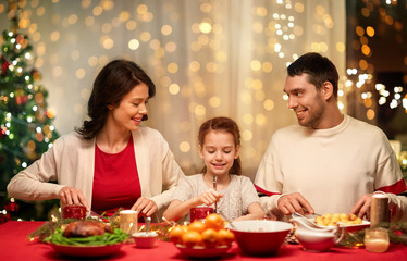 holidays, family and celebration concept - happy mother, father and little daughter having christmas dinner at home