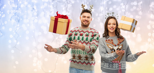 people and holidays concept - portrait of happy couple with christmas gifts at ugly sweater party over festive lights background