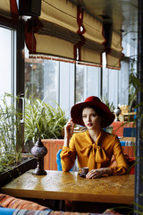 girl in a cafe with a cup of coffee and a hat.portrait of sensual young girl wearing floppy hat and blouse with bow. Beautiful brunette woman in cafe holding cup of coffee