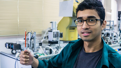 A young Malay engineering student with spectacles holding a screwdriver working in the lab.