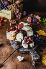 assortment of cheese on wooden board with fruits, honey and ham on brown wooden table, selective focus
