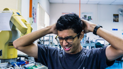 A young Malay engineering student with spectacles thinking hardly by holding head.