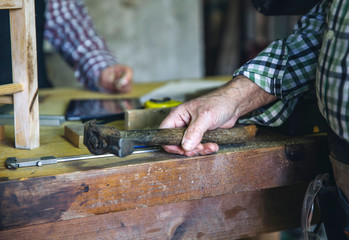 Detail of carpenter's hand holding a hammer leaning on the workbench