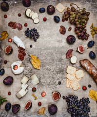 assortment of cheese with figs, grapes, ham and crackers on shabby background, top view