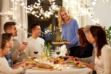 celebration, holidays and people concept - happy woman offering roast chicken to family having...