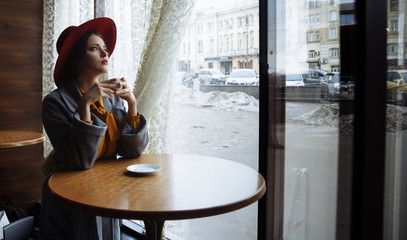 girl in a cafe with a cup of coffee and a hat. beautiful girl with a cup of coffee at the window in a cafe, waiting for a meeting, breakfast