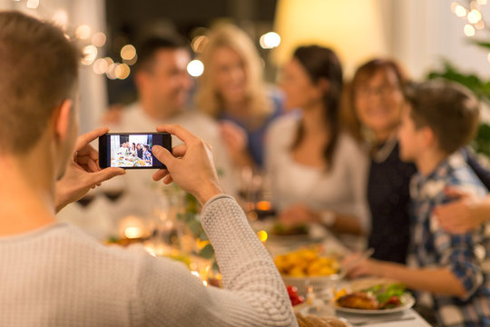 celebration, holidays and people concept - man with smartphone taking picture of family at dinner party