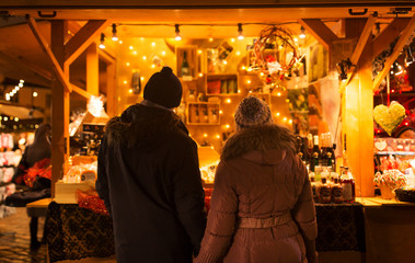 love, winter holidays and people concept - happy senior couple at christmas market souvenir shop stall in evening