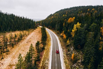 Fototapeta na wymiar Aerial view of first snowy autumn color forest in the mountains and a road with car in Finland Lapland.
