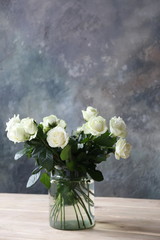 a bouquet of white roses in a glass vase in a room with a concrete gray wall