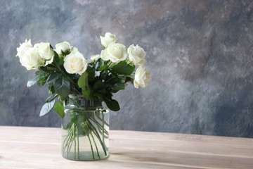 a bouquet of white roses in a glass vase in a room with a concrete gray wall