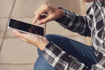 Woman hand holding and touch mobile phone sitting in the outdoor