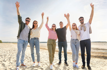 friendship, leisure and people concept - group of happy friends waving hands on beach in summer