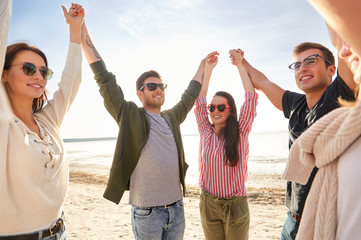 friendship, leisure and people concept - group of happy friends holding hands on beach in summer