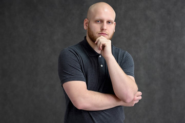 Portrait of a handsome bald man in a gray t-shirt on a gray background in the studio. Shows emotions in various poses.