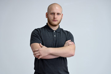 Portrait of a handsome bald man in a gray t-shirt on a white background in the studio. Shows...