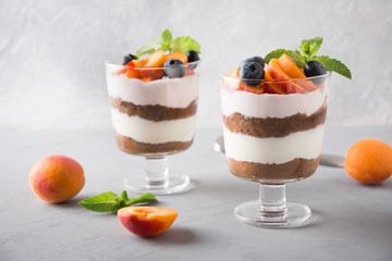Apricot trifle, chocolate biscuit, layered dessert with fresh berry and gentle cream cheese on grey.
