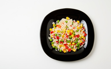 Top view of a black plate with a mixture of rice, sweet corn and fresh organic vegetables fried in sunflower oil with copy space. Rice, sweet corn, sweet red pepper, green pea. Healthy vegan diet food