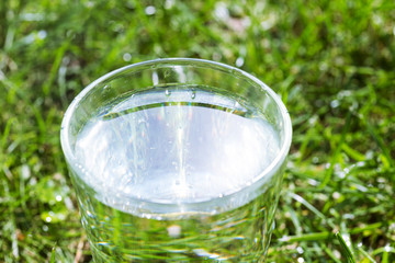 A glass of clean transparent drinking water on a grass background.