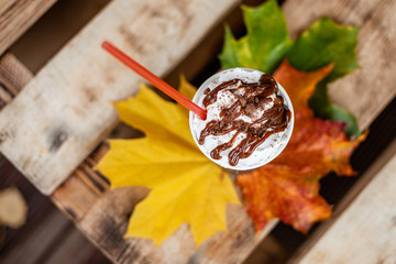 Autumn composition still life. Cup of coffee latte with cocktail straw and autumn colored leaves on wooden board with. View from above