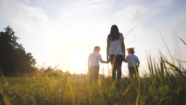 happy family funny walking go for are hold hands a teamwork Silhouette. happy little children boy and girl with mother family at sunset. mom and son mom daughter and son in white t-shirts walk on the