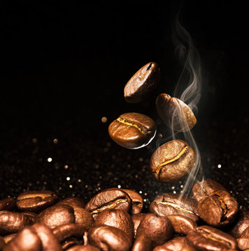 Roasted coffee beans. Seeds of freshly roasted coffee with smoke. Coffee beans closeup with emphasis on the grain with smoke.