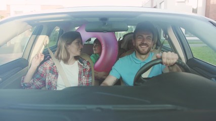 Front view of pretty married cuple and their kids riding a car in the city. Cheerful dad and his children giving high five having fun in the car during a family roadtrip to the seaside.