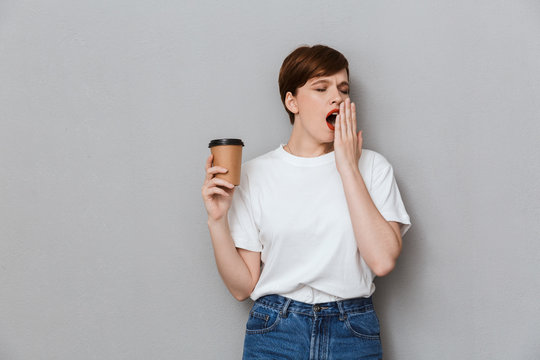 Image of sleepy brunette woman yawning and holding takeaway coffee cup
