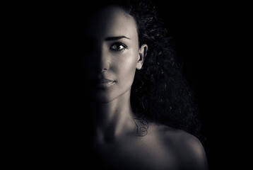 Beautiful young woman with curly hair looking sexy with half shadow on the face. Closeup portrait. Black and white Photography. 