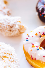 Assorted multicolored donuts in a bakery box with chocolate frosted, glazed and sprinkles donuts. Sugar addiction or festive menu concept.