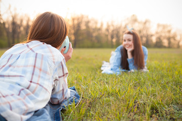Two young women lie on the grass and shooting photos.