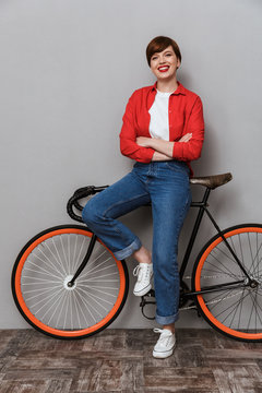 Full length image of happy woman smiling and standing by bicycle