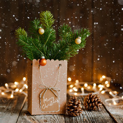 Christmas composition. Paper bag with and bumps fir branches on brown wooden background and bokeh...