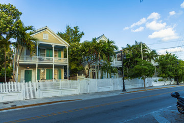 View of one of streets of Key West. Old houses and big green trees on blue sky background. Key...