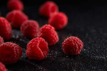 Fresh ripe raspberries on a black surface with drops of water.