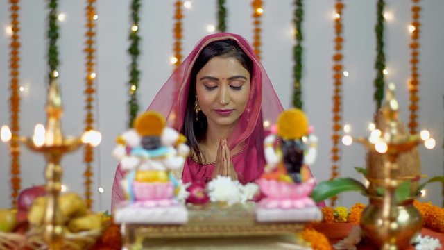 Pretty Indian female praying in front of Hindu gods Lakshmi and Ganesh on Diwali. Bokeh shot of a young woman doing Diwali Puja in the temple of  Lord Ganesha and Goddess Lakshmi with colorful Diwa...