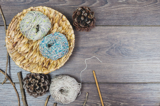 Basket with balls of wool in natural tones, pinecorns and needles on a wooden background