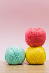 Three stacked balls of wool in yellow, blue and pink in a wooden table and pink background