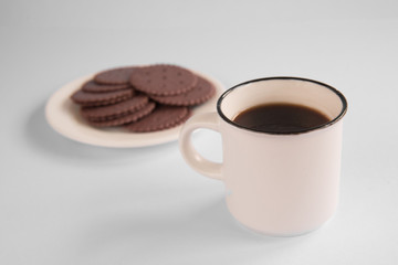 A white Cup of coffee stands on a white background. Chocolate cookies are on the plate. light breakfast.