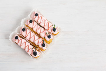 Tasty French eclairs with cream and fresh berries on white wooden table. Set of delicious eclairs.