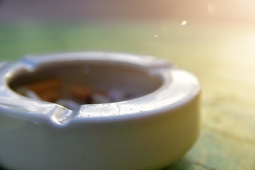Close-up the ashtray on the light green table and yellow light at morning time.