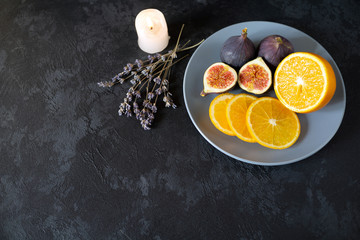 Fototapeta na wymiar gourmet dish with exotic fruits, orange and figs on a gray plate on a black background