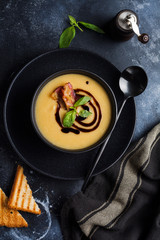 Potato soup cream with bacon and soy sauce in black bowl, on dark old concrete background. Top view.