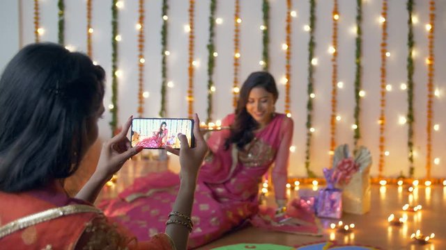 Beautiful Indian females celebrating Diwali festival while clicking pictures - festive background. Bokeh shot of younger and older sisters having fun on Diwali  taking photos with a smartphone in t...