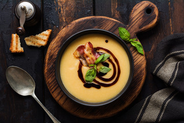 Potato soup cream with bacon and soy sauce in black bowl, on dark old concrete background. Top view.
