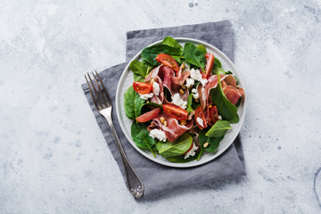 Spring Salad with spinach, cherry tomato, mozzarella, pine nuts and ham with olive oil in a simple...